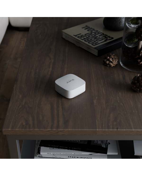 Balts gaisa kvalitātes sensors ar digitālo displeju un vadības pogām, novietots uz koka virsmas.